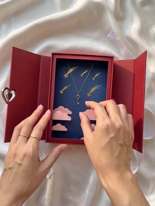 Hands opening a red gift box holding a silver necklace