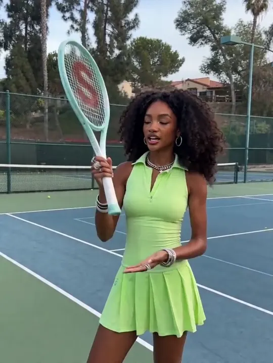 A tennis player in green kit talking to camera on a court