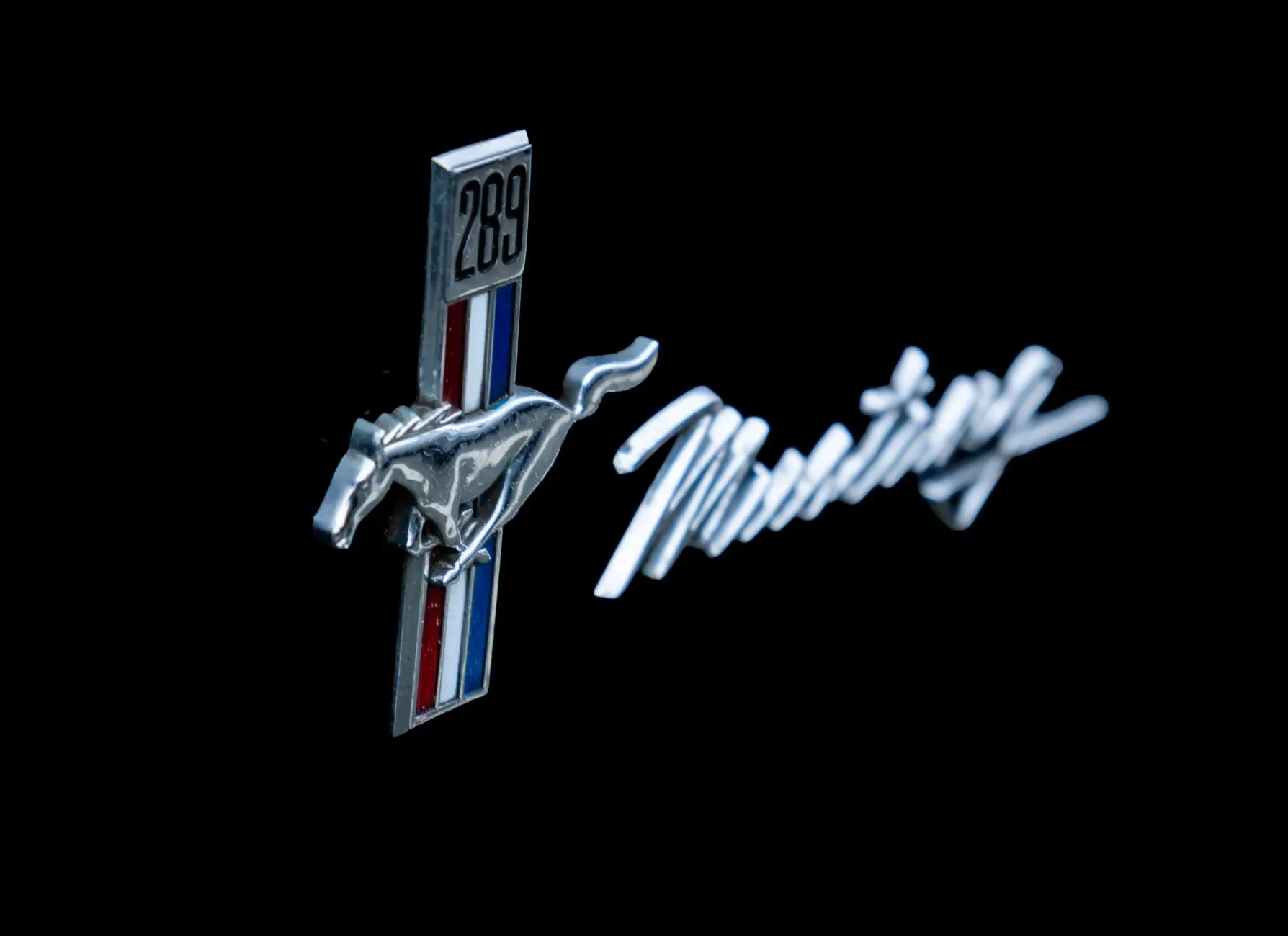Close-up of a vintage Mustang emblem with a 289 badge on a dark background.